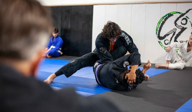Two people practice jiu-jitsu in a gym.