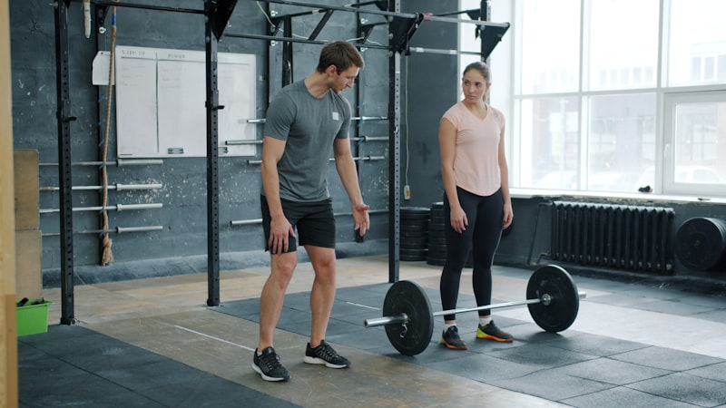 A man and woman with a barbell in a gym.