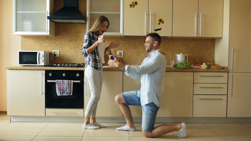 Man proposes to surprised woman in modern kitchen.