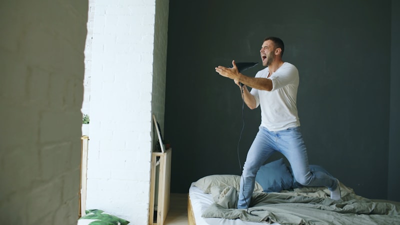 Man jumping on bed singing into remote control