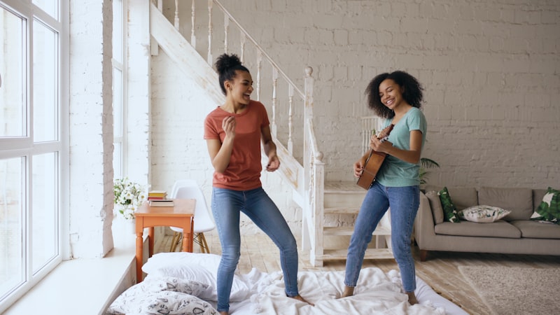 Two women dancing and playing ukulele on bed