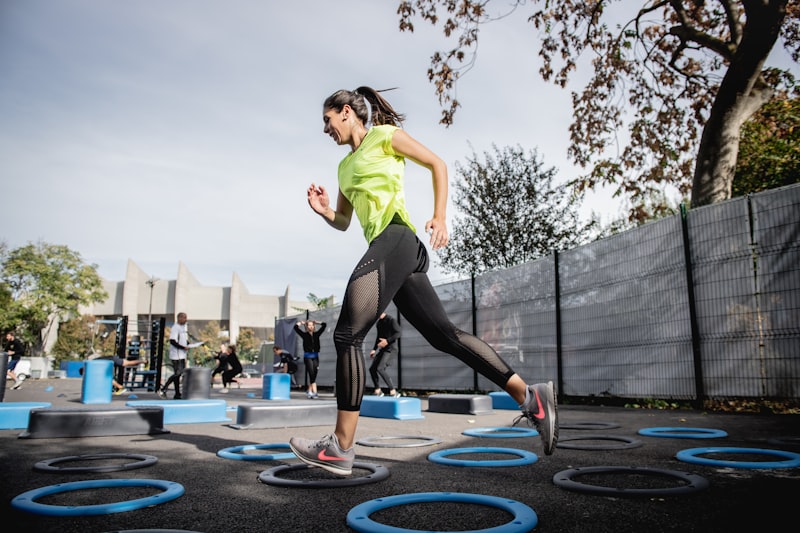 woman in green tank top and black leggings doing yoga on blue round trampoline