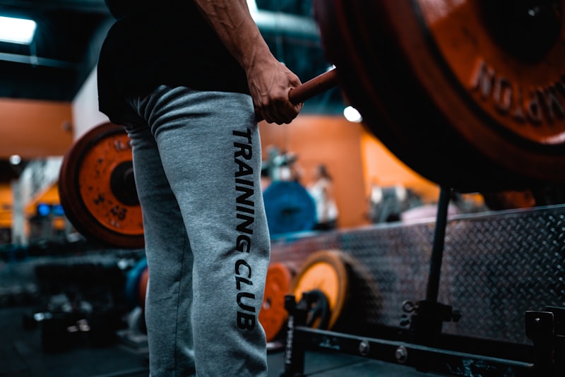 man in black tank top and blue denim jeans holding black and brown barbell